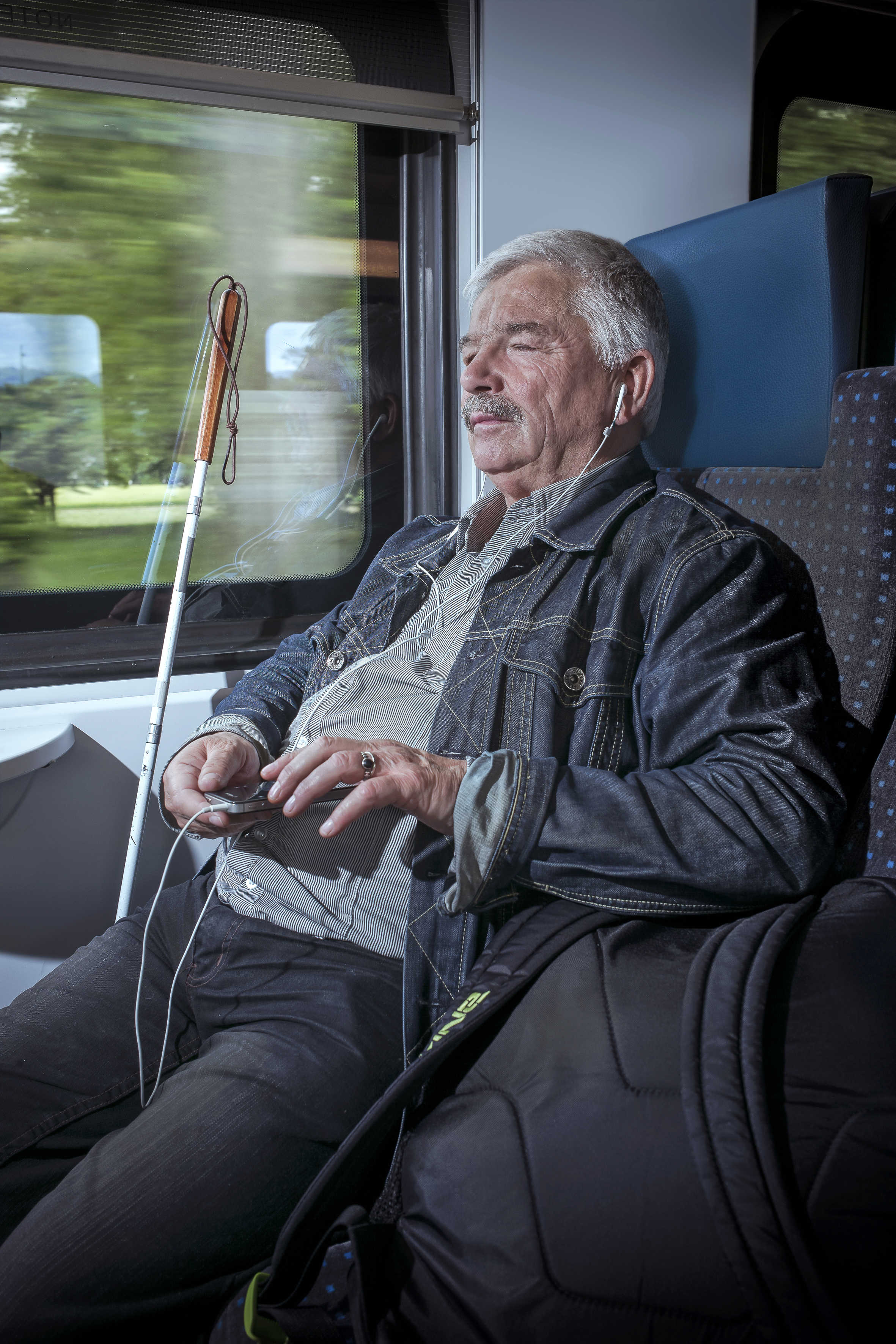homme aveugle dans un train CFF écoutant un livre audio depuis son smartphone